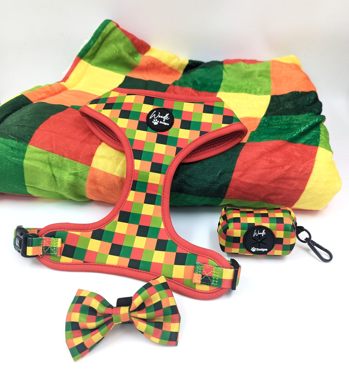 A pet accessory set featuring a checkered harness, matching bow tie, and small zippered pouch, all in green, yellow, and red checkered pattern on a white background. Ireland, UK and Worldwide. 