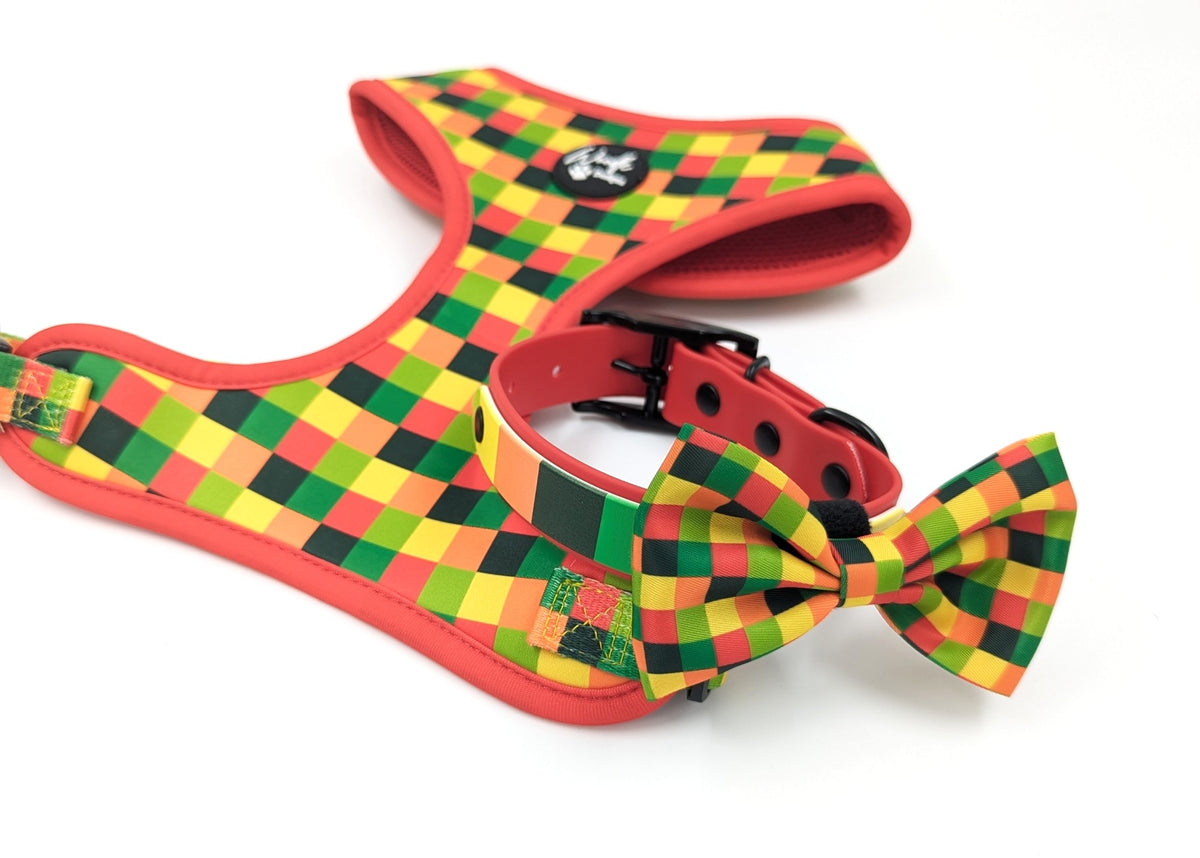 An adjustable dog harness and matching collar with a matching dog bow tie set, featuring a vibrant red, green, and yellow checkered pattern on a white background. Ireland UK and worldwide.