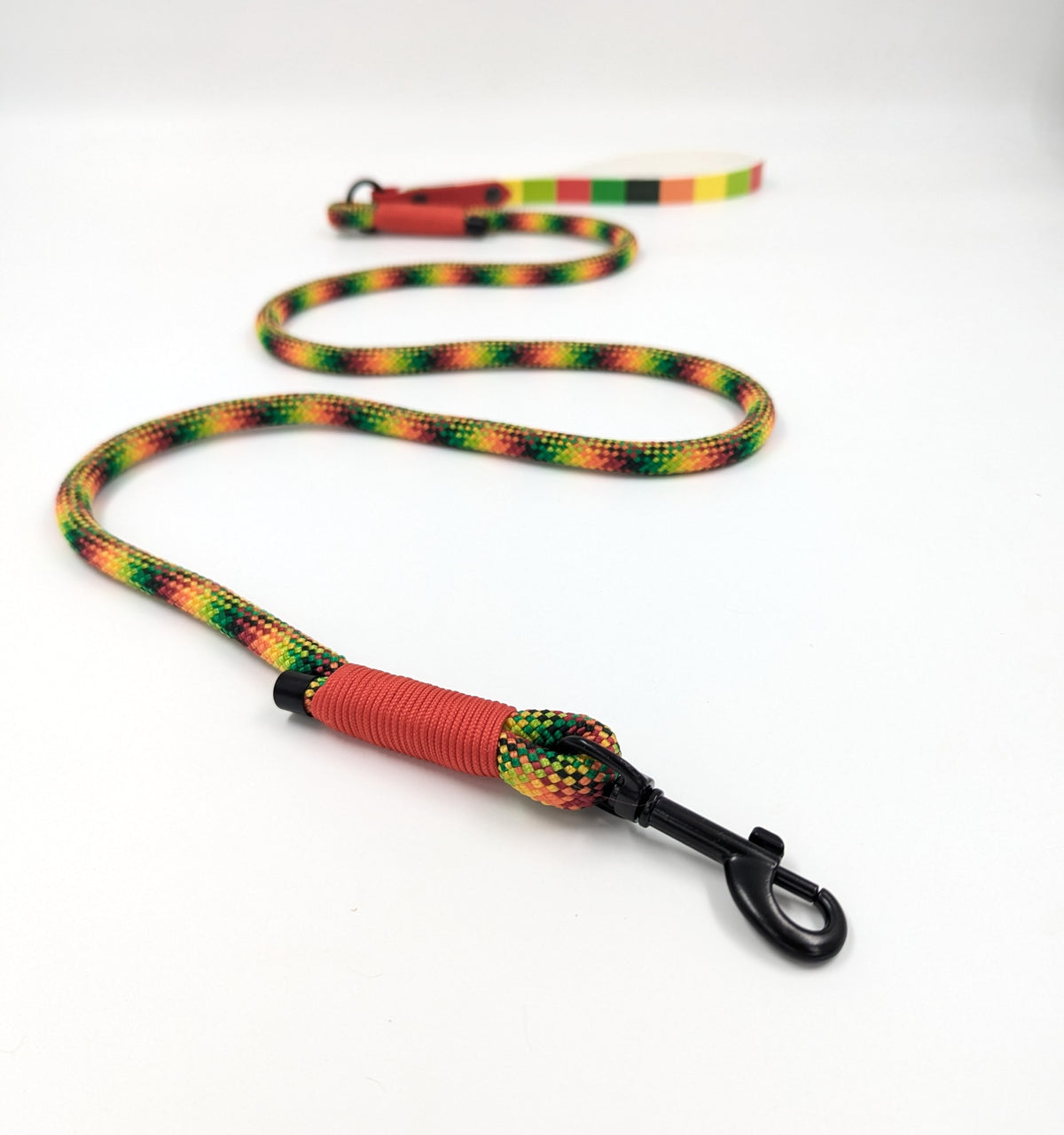 A handmade rope dog leash with UV printed BioThane handle and black metal clip, featuring a repeating green, yellow, orange, and red pattern on a white background. Ireland and worldwide. 